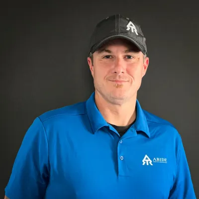 Joe Williams, Co-Owner. Headshot in blue polo with gray background.