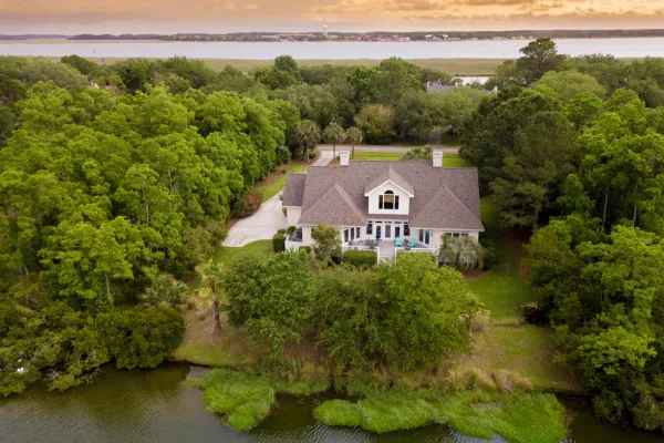 Tan home with Light Brown Shingles in the middle of heavily wooded property.