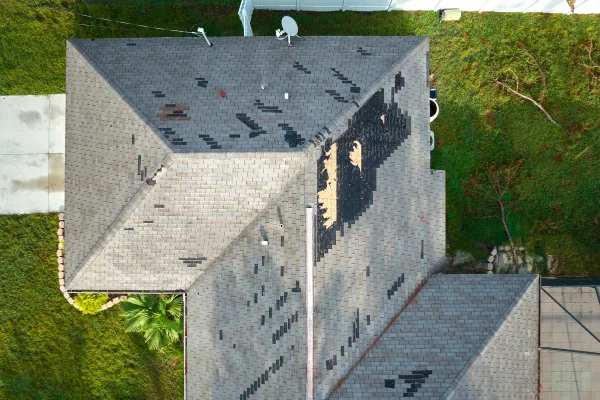 Residential roof in need of tarping. Image is taken from above the home showing missing shingles and underlayment on the roof.