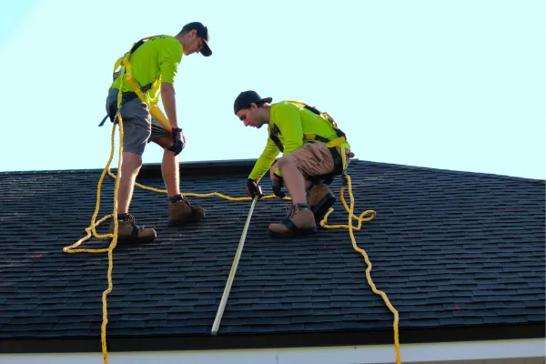 Two-man roofing team tied off on a roof taking measurements.